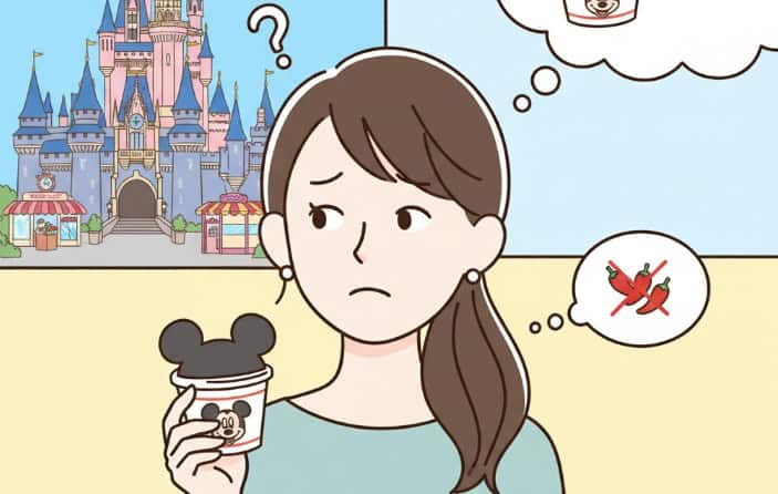 ディズニーリゾートのシンデレラ城を背景に、ミッキーマウスのカップラーメンを手に持ち、美味しいのか悩んでいる日本人女性のイラスト。女性の頭上には、美味しい顔と美味しくない顔の絵文字があり、カップラーメンの味について考えている様子が描かれている。